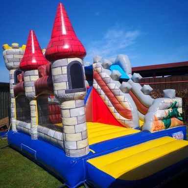 Buntes Hüpfburg-Schloss mit Rutschen und Türmen auf Rasenfläche.