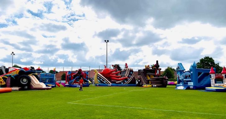 Bunte Hüpfburgen und Rutschen auf einem grünen Rasenplatz unter bewölbtem Himmel.